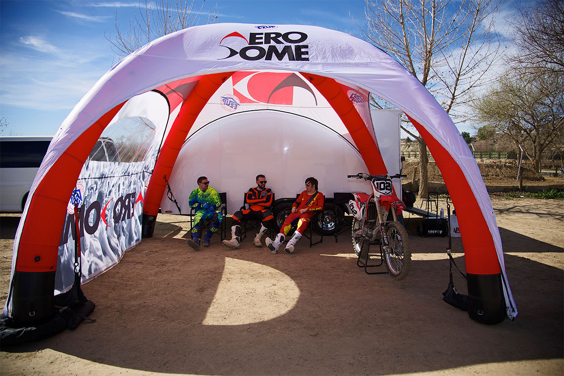 отбор мотористи си почива под червена надуваема шатра E-Z UP Aero Dome™