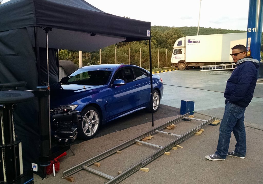 Плътна черна шатра E-Z UP® на снимачната площадка с фарт и нов модел синьо BMW